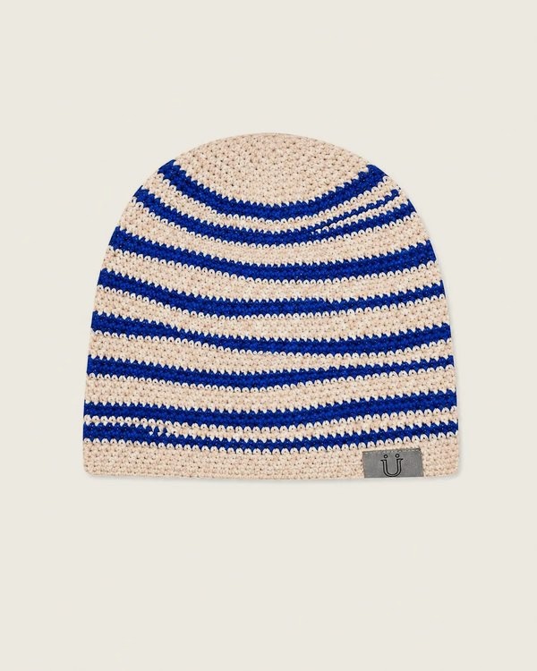 A hand-crocheted beanie in cream with cobalt blue stripes and a woven Ü tab at the hem.