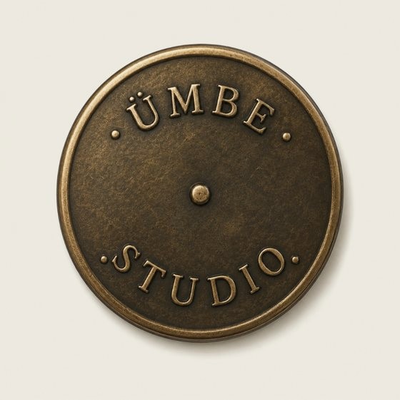 A cast bronze disc with ÜMBE curved across the top and STUDIO across the bottom, struck into the metal around a central rivet.