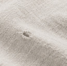 A close-up of the same jersey along a seam, showing the slub texture and a small worn hole.