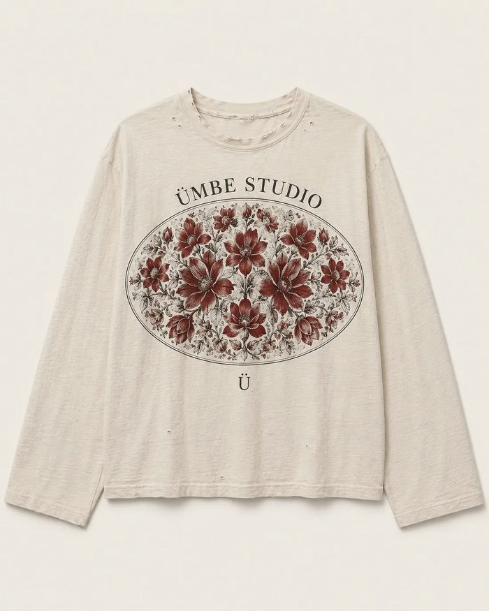 A distressed cream long-sleeve tee printed with a dark red engraved floral oval, ÜMBE STUDIO curved above it and a small Ü below.