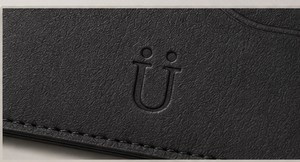 The Ü blind-debossed into black leather, catching the light only at the edge of the stroke.