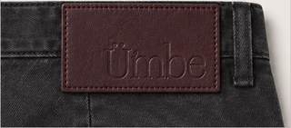 An oxblood leather patch debossed ümbe, stitched at the back waistband of the charcoal twill pant.