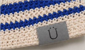 A small grey woven tab carrying the Ü, stitched into the hem of the cream and cobalt crochet beanie.