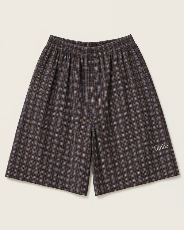 Long pleated shorts in a brown and cobalt check, with a small embroidered Ümbe wordmark at the hem.
