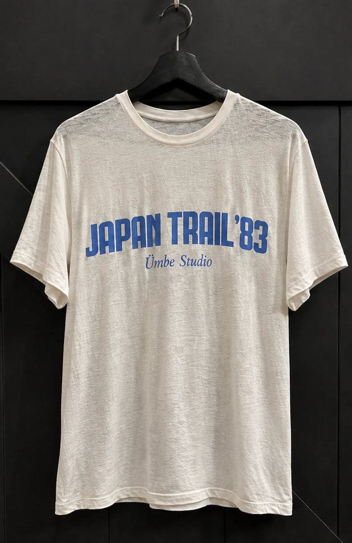 The printed tee on a hanger against a black wall, showing the full garment and its shorter, boxier cut.