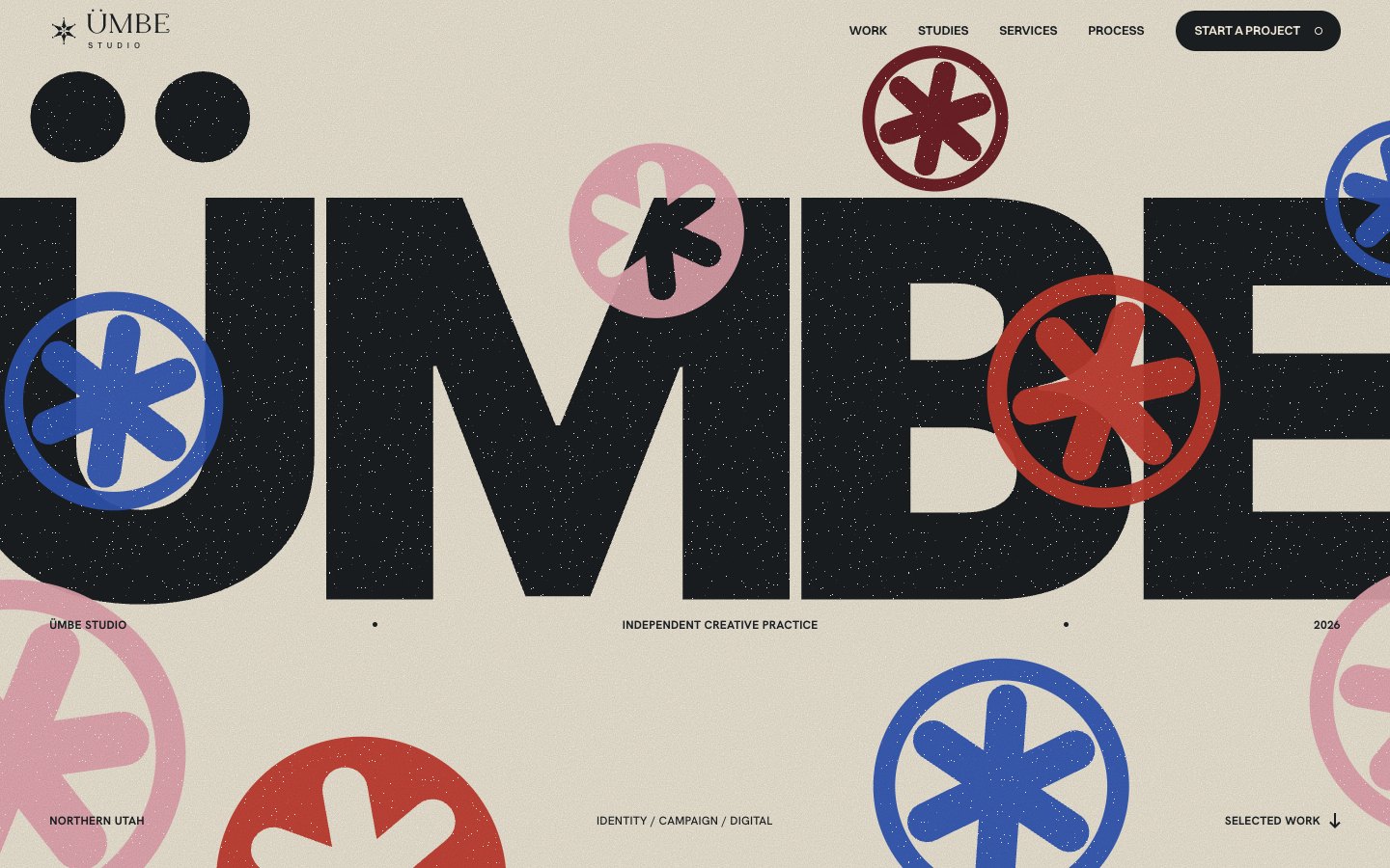 Round one: the word ÜMBE in heavy black capitals across a beige field with red, blue and pink asterisk stamps over it. It reads as a website headline.